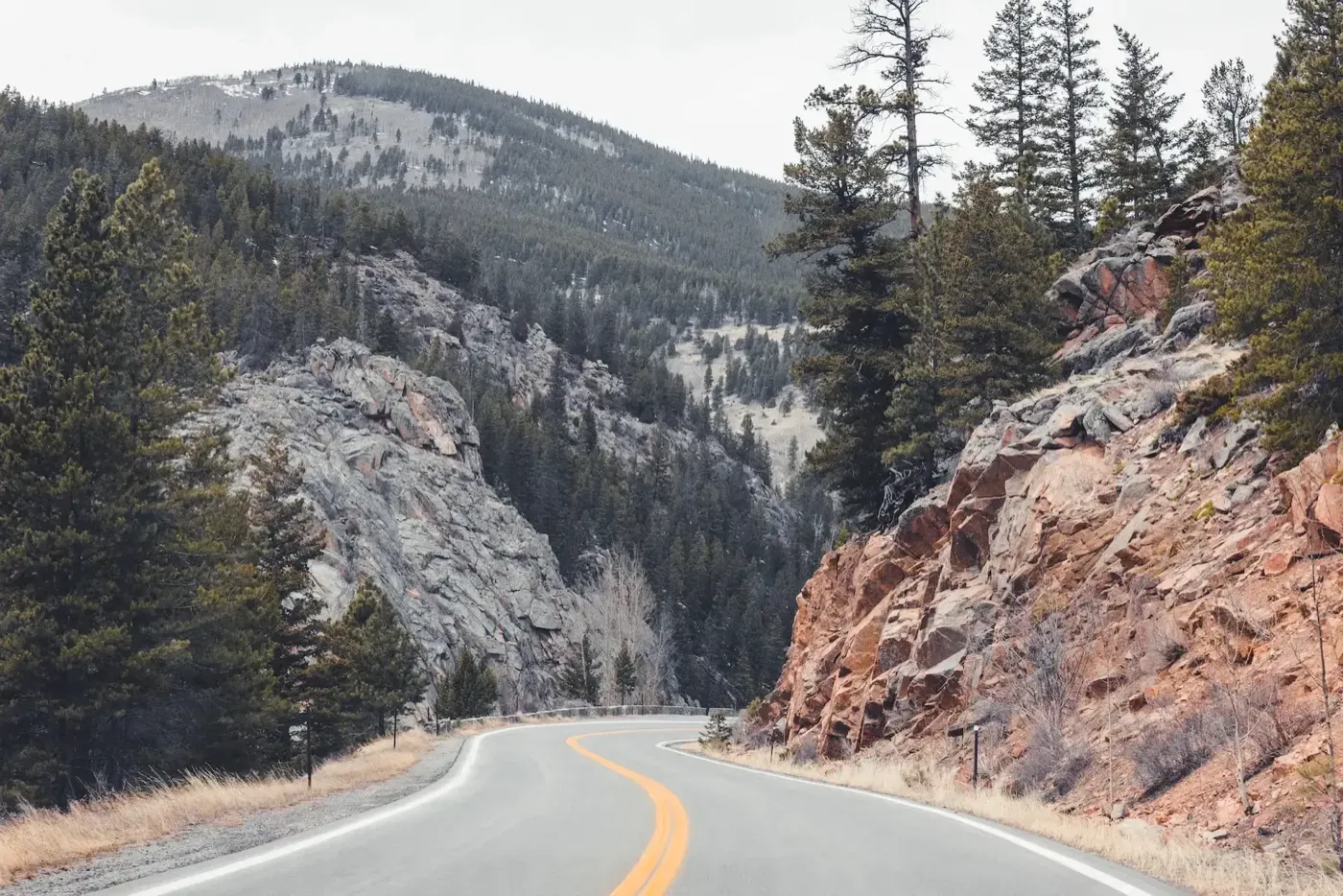 Two-lane road curving through a rocky canyon lined with pine trees.