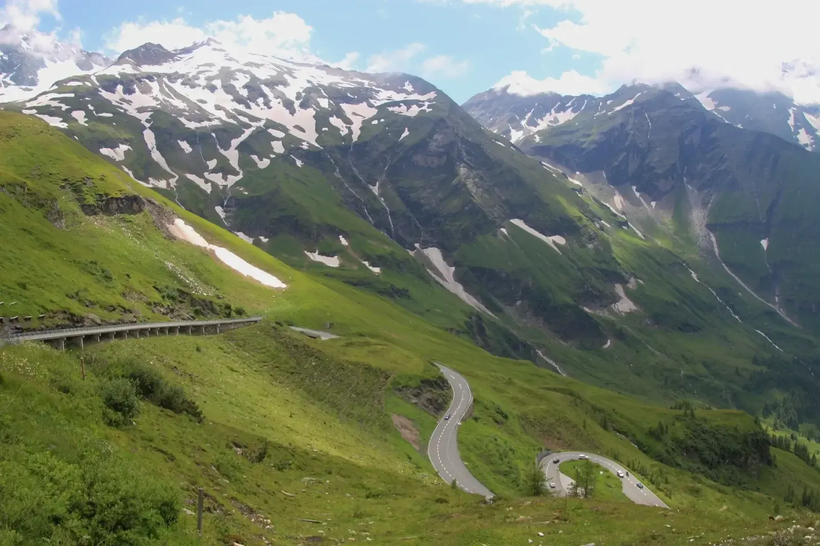 Grossglockner High Alpine Road winding up green slopes beneath snow-streaked mountains.
