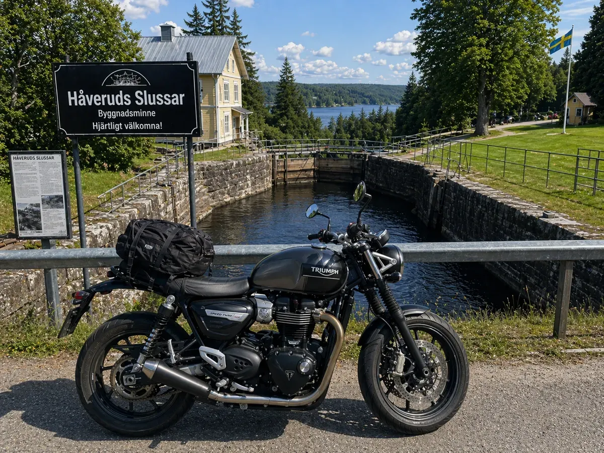 Svart Triumph-motorcykel parkerad vid slussen i Håverud, med skylten Håveruds Slussar bakom.