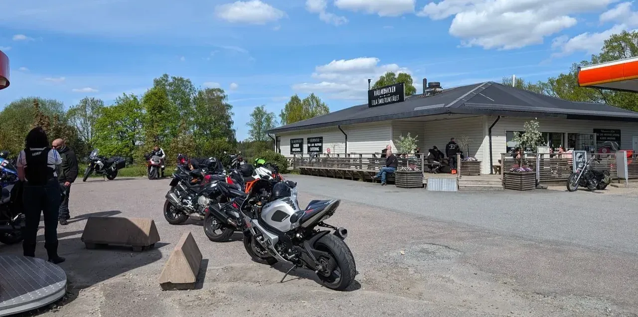 Motorcyklar parkerade på grusplanen utanför den vita kafébyggnaden vid Källarbacken, med folk på terrassen.