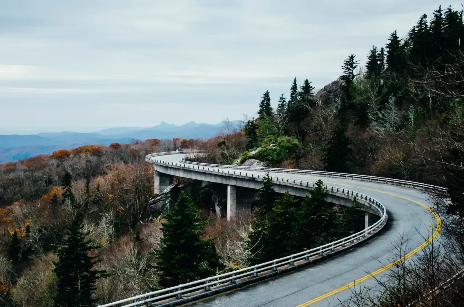 The Linn Cove Viaduct curving around a forested mountainside in autumn, with blue ridges beyond.