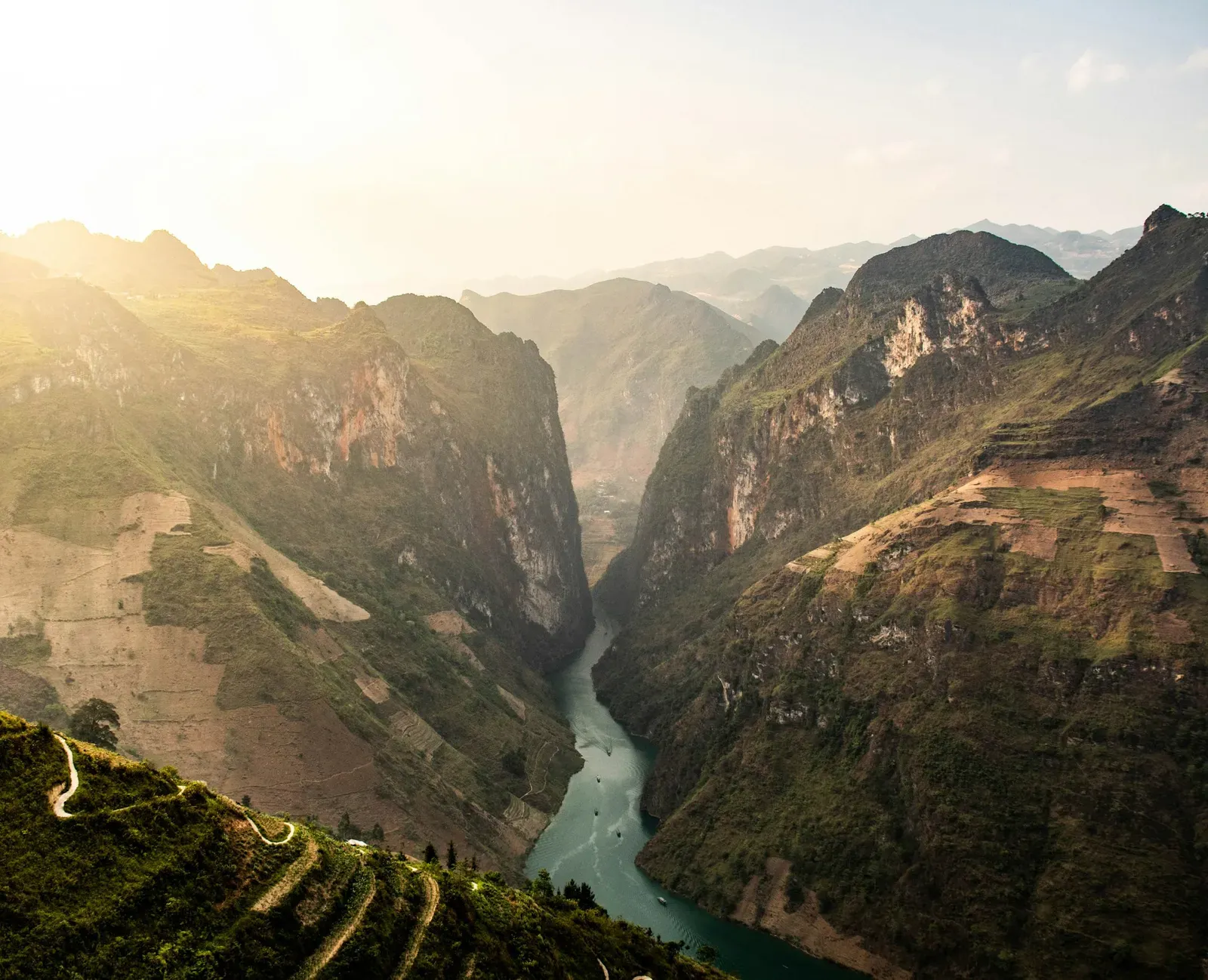 River winding through a deep mountain gorge in hazy sunlight, with a road along the slope.